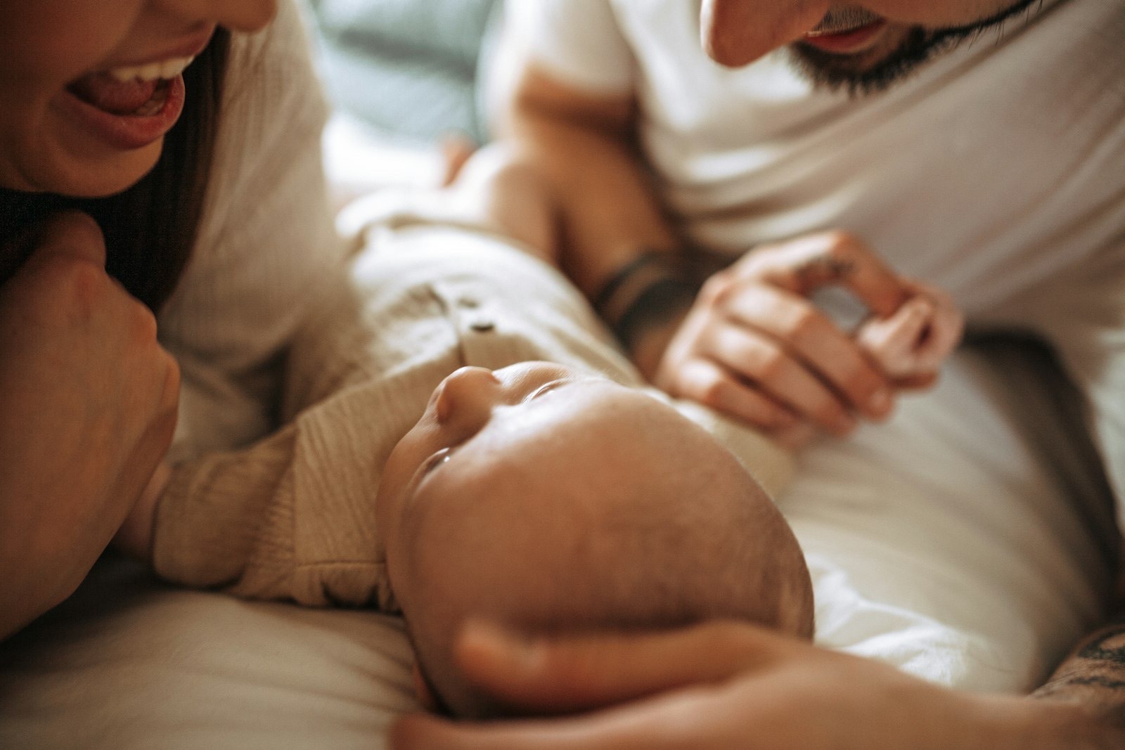 New parents lean close over their baby on soft cream bedding.