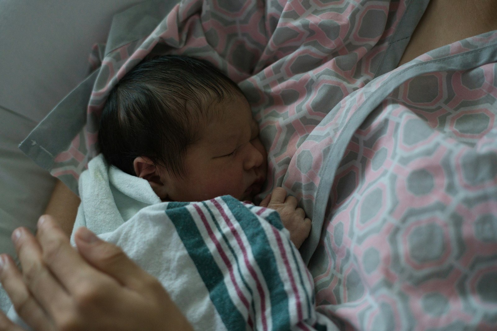 A newborn rests against a parent in soft pink light.