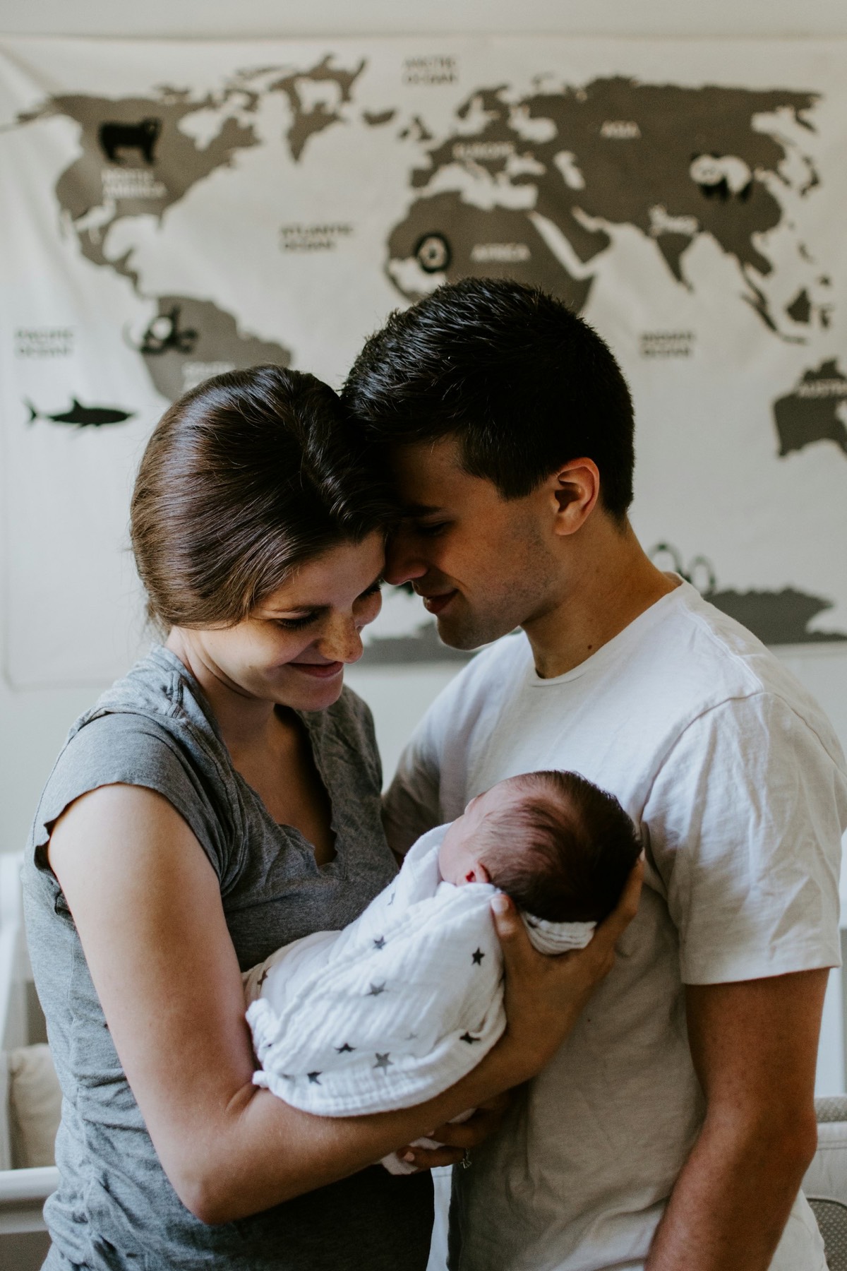A couple stands forehead to forehead, cradling their newborn between them.